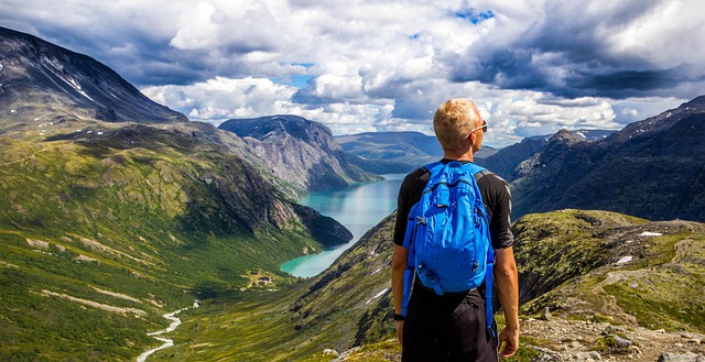 Vaeltaja katsoo vuoristomaisemaa sininen reppu selässään